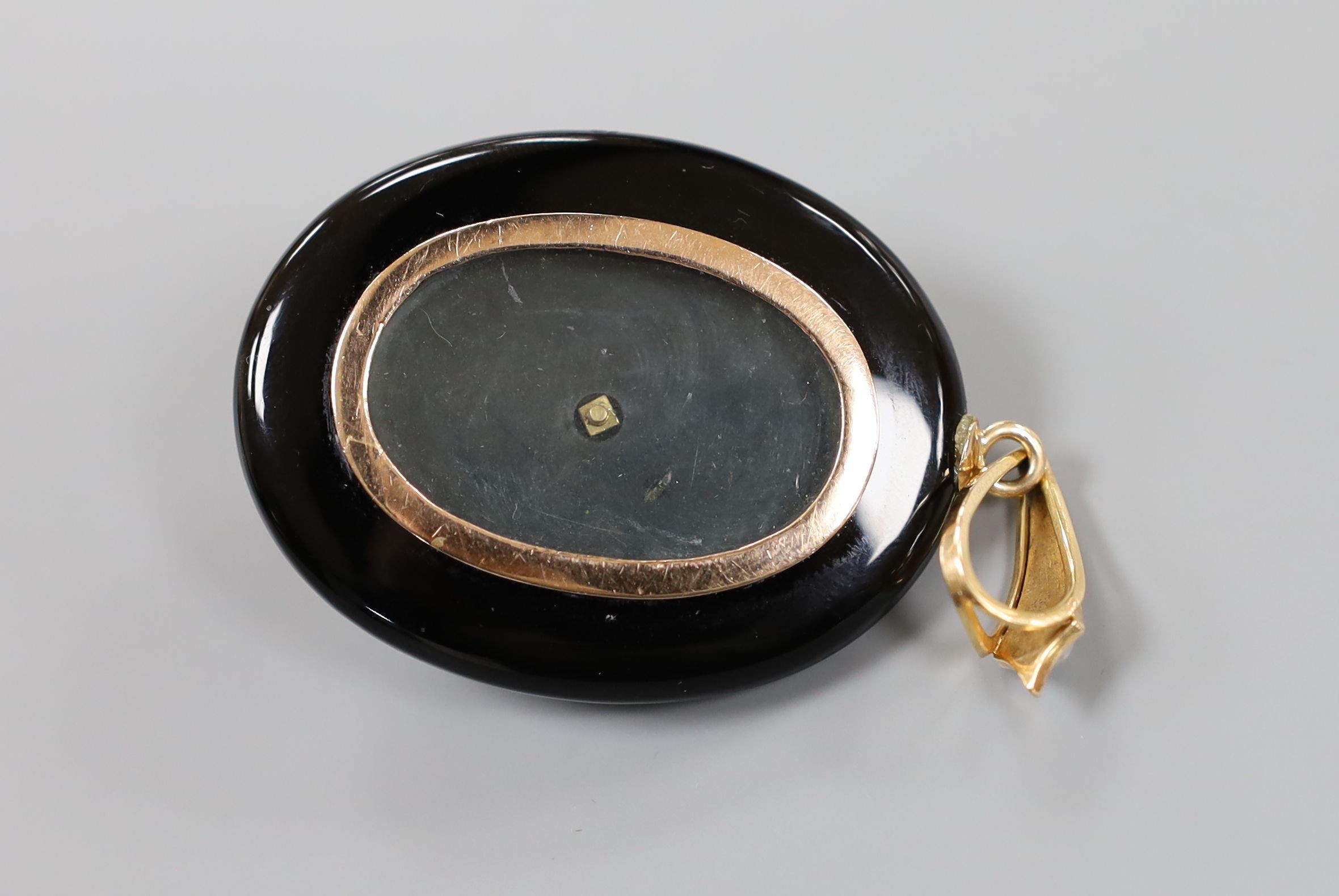 A Victorian black enamel, rose cut diamond, ruby coloured paste and seed pearl set oval mourning pendant, with glazed back and seed pearl set yellow metal bale, overall 69mm.